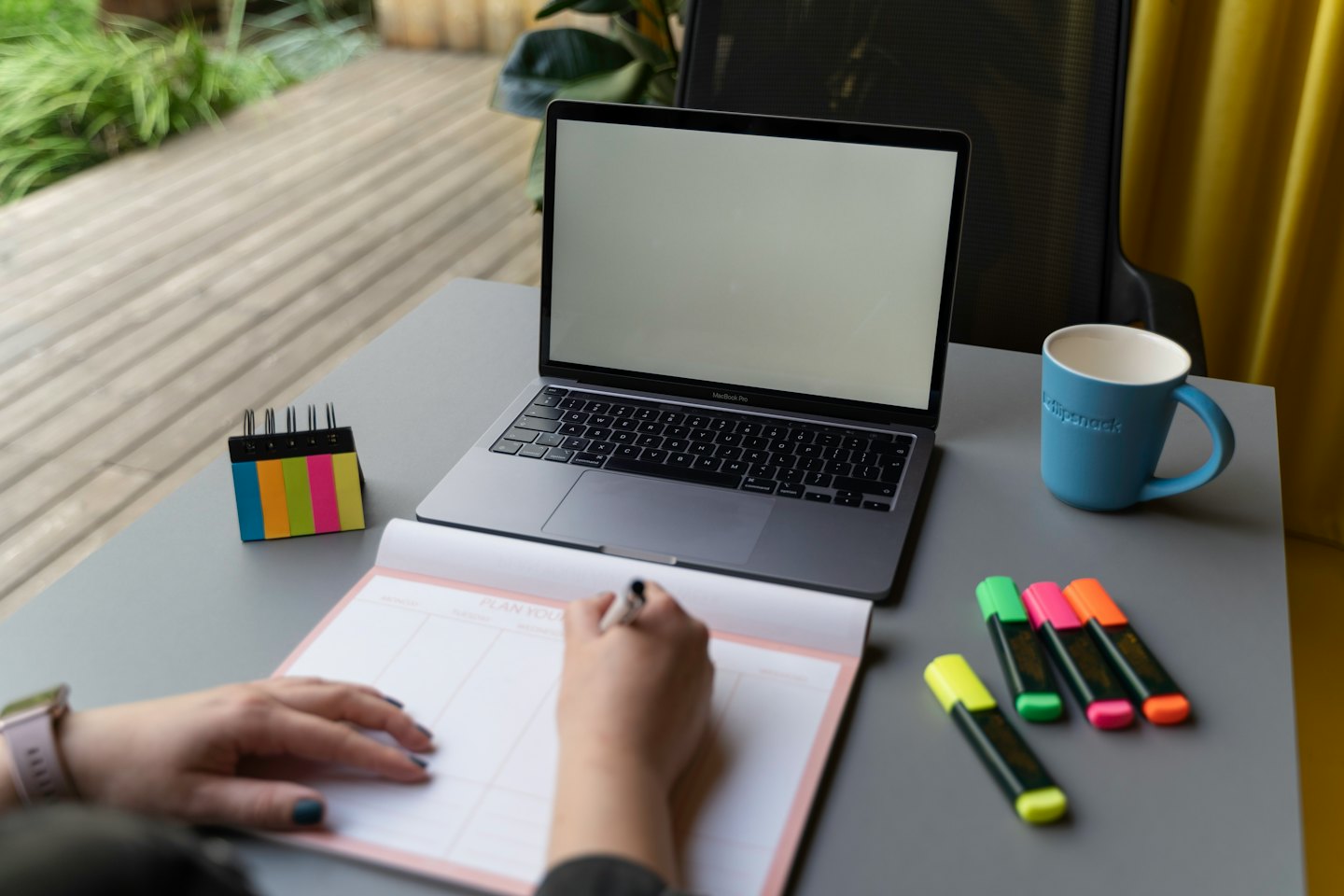 Mani che scrivono su un'agenda accanto a un laptop aperto.